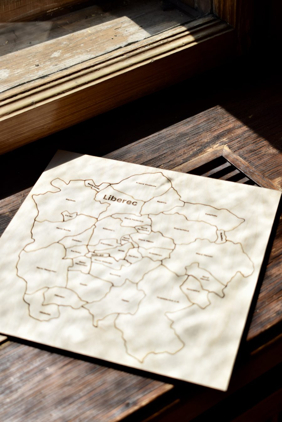 Celé puzzle Liberce v podvečerním slunci u okna – čtvercová deska s mapou města a nápisem Liberec.